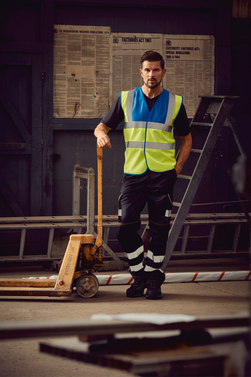 gilet bicolore bleu royal et jaune fluo haute visibilité avec bandes réfléchissantes sans manches fermeture velcro porté par un homme avec un pantalon noir