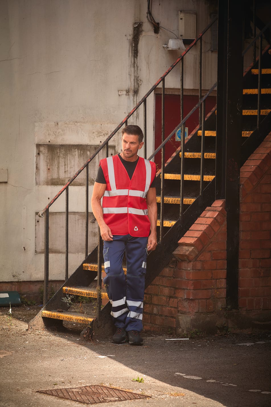 gilet sans manches rouge avec bandes réfléchissantes haute visibilité porté par un homme avec un pantalon bleu