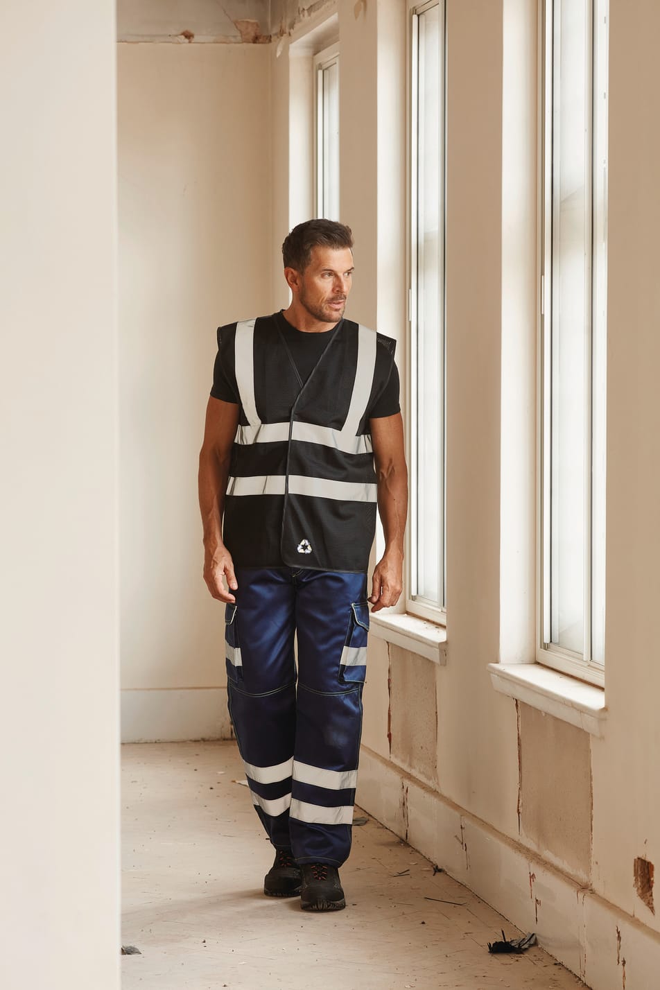 gilet sans manches noir avec bandes réfléchissantes haute visibilité porté par un homme avec un pantalon bleu