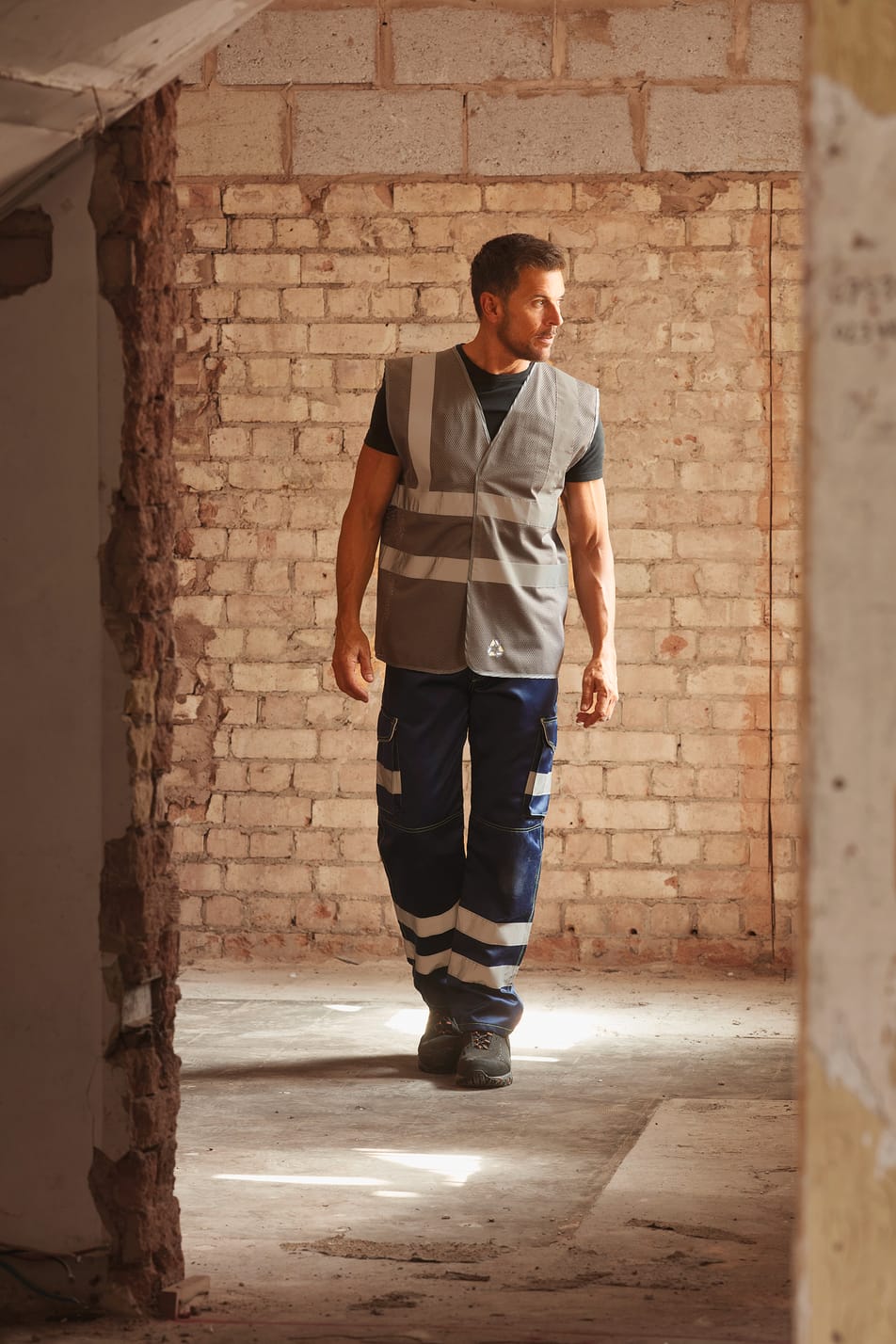 gilet sans manches gris avec bandes réfléchissantes haute visibilité porté par un homme avec un pantalon bleu